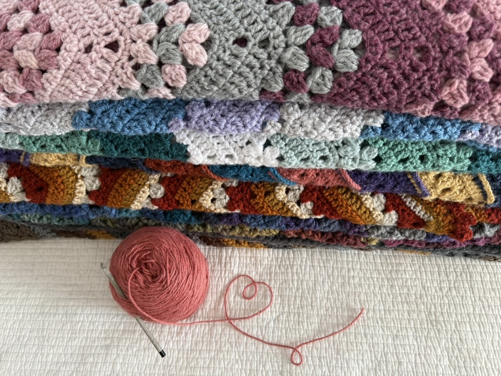 Stack of colorful crochet blankets, yarn and hook, heart shape