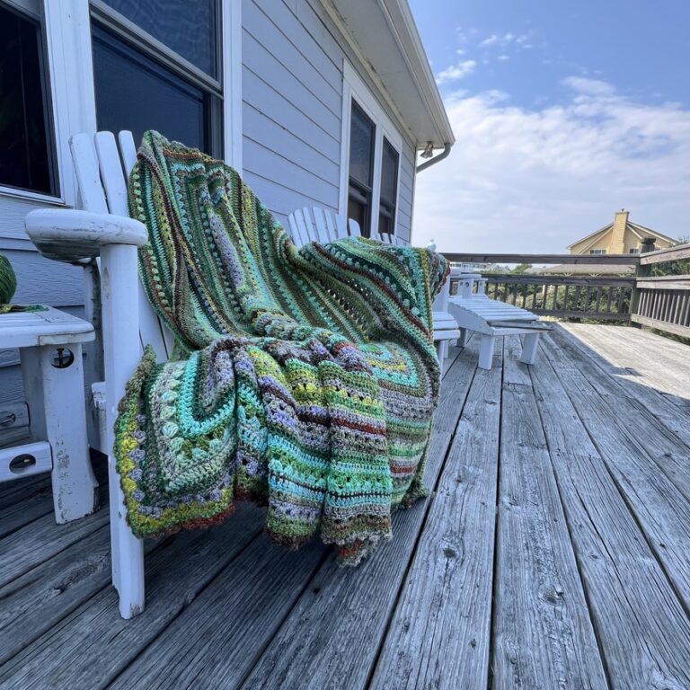 6-Day Great Granddaddyo Blanket featuring Noro Yarn draped on a chair on the front of a beach house