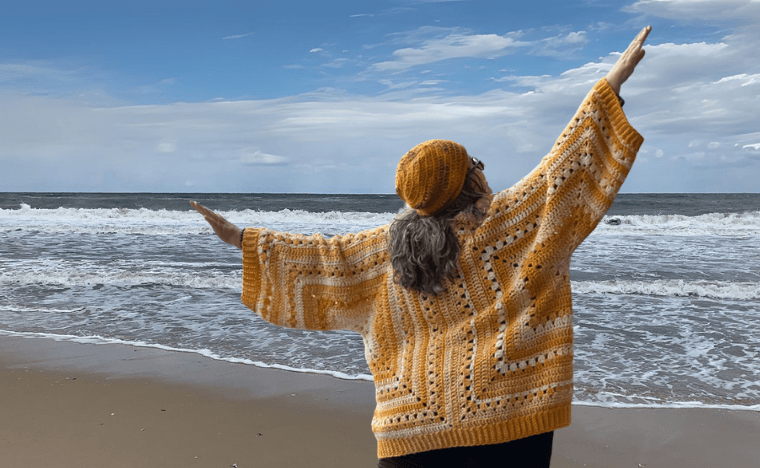 Betty McKnit dancing in a 6-Day Hexagon Cardigan and Invisible People Hat at the beach.