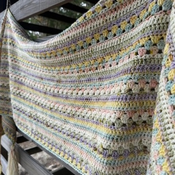 Decorative image pastel colored crochet shawl hanging on wooden siding outdoors.